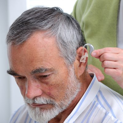 person placing hearing aid in a man's ear